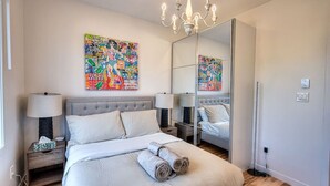 A modern bedroom with a large bed, two bedside tables, a chandelier, and a mirror.