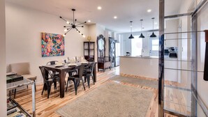 A modern dining area with a wooden table and chairs, a colorful abstract painting, and a contemporary chandelier.