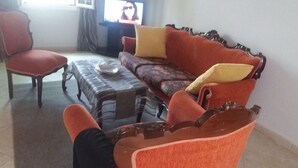 A living room with a red sofa, a matching armchair, and a coffee table. A television is mounted on the wall. - Maria House in the port of Kalymnos (Kalymnos)
