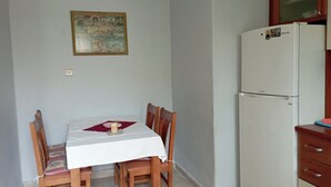 A dining area with a table set for four, a refrigerator, and a wall-mounted picture. - Maria House in the port of Kalymnos (Kalymnos)