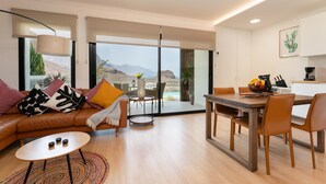 Un salon moderne avec un canapé, une table basse et un coin repas. De grandes portes vitrées offrent une vue sur les montagnes.