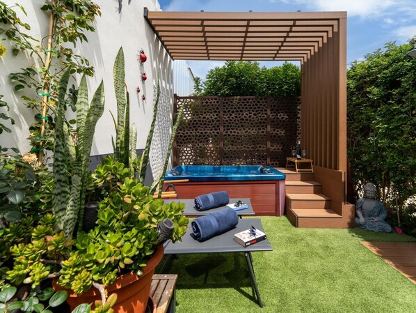 Un espace de détente extérieur moderne, doté d’un jacuzzi, de sièges et d’une végétation luxuriante.