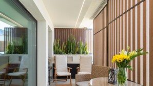 Un espace extérieur moderne, aménagé avec des chaises en osier et une table en verre, un mur à rayures verticales et une plante en pot.