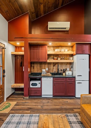 A compact kitchen with wooden cabinets, a built-in oven, a dishwasher, and a refrigerator. - Comfy Cabin w/ Pickleball, Golf, Sauna & Hot Tub! (Bloomington Springs)