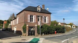 Une maison à deux étages en briques, avec des volets blancs, une piste cyclable verte qui la traverse et un ciel dégagé.