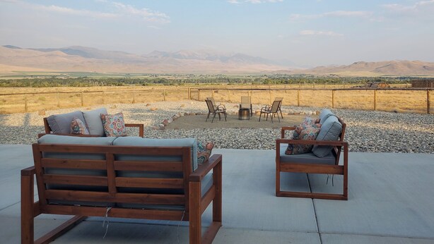 Un patio con dos bancos de madera y una mesa, con vistas a un paisaje desértico con montañas a lo lejos.