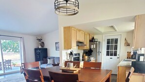 Un comedor con mesa y sillas de madera, una lámpara colgante y una cocina al fondo.