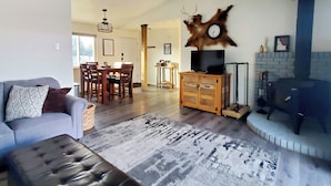 Una sala de estar con sofá, reposapiés y alfombra estampada. Hay un comedor con sillas y mesa, y una chimenea con repisa de piedra.