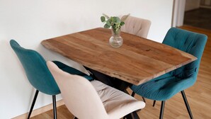 A wooden dining table with a vase of green foliage, surrounded by teal and beige upholstered chairs.