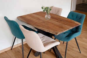 Ein Holzespeisesaal mit einer Vase mit Grünpflanzen, umgeben von stuhlförmigen Sitzgelegenheiten in Türkis und Beige.