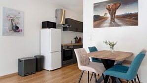 A compact kitchen with a microwave, oven, and a small refrigerator. There is a dining table with chairs and a vase with flowers.