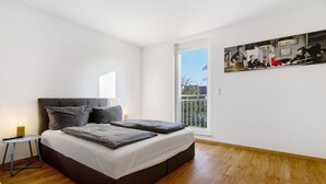 Un dormitorio moderno con una cama grande, una mesita de noche pequeña, una ventana con vistas y una obra de arte colgada en la pared.