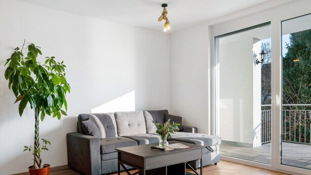 Una sala moderna con un sofá seccional gris, una mesa de centro, una planta en maceta y un ventanal corredizo que da a un espacio exterior.