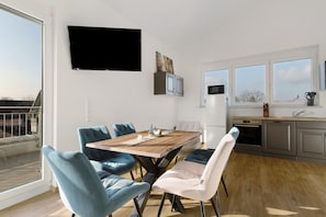 A modern kitchen with a dining area, large windows, and a flat-screen TV.
