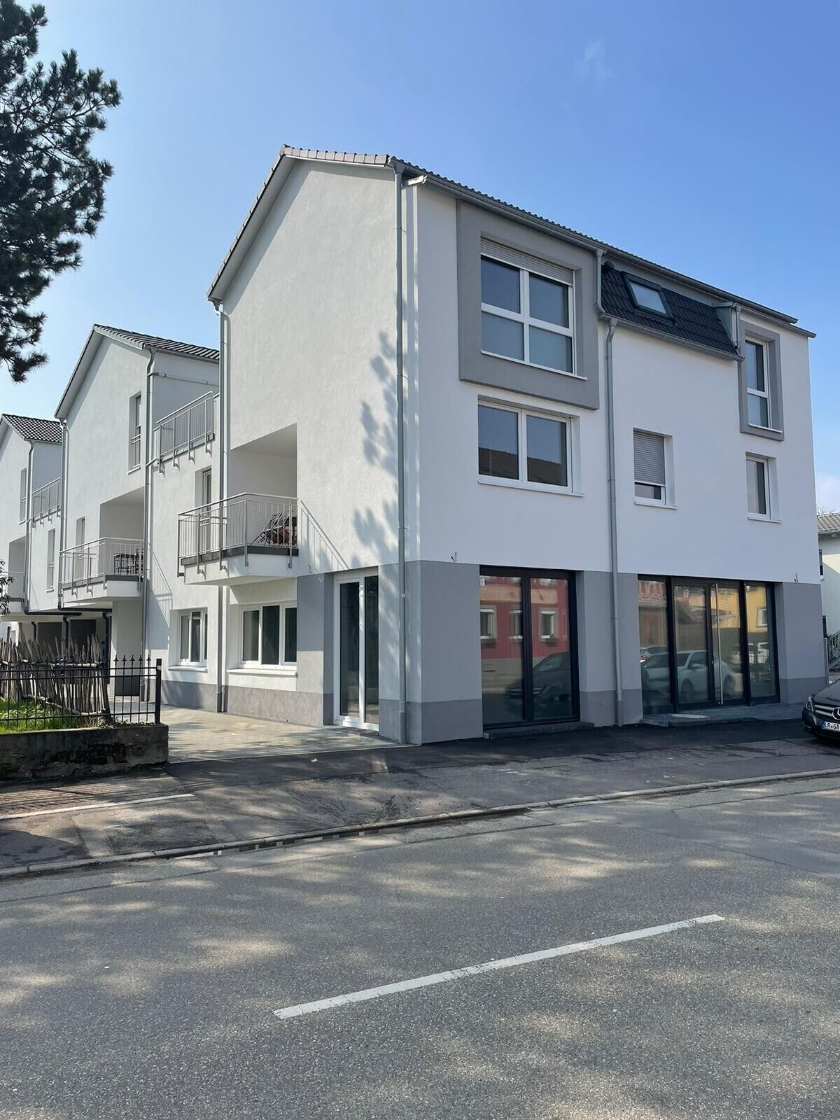 A modern two-story building with a flat roof, large windows, and a visible balcony.