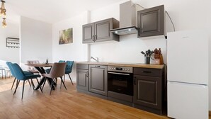 A modern kitchen with dark cabinets, a built-in oven, and a white refrigerator.