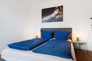 Un lit avec une literie bleue, un tableau au mur et des lampes de chevet.