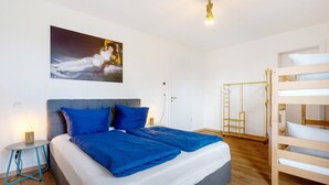 A bedroom with a bunk bed, a bedside table with a lamp, a painting on the wall, and a wooden floor.