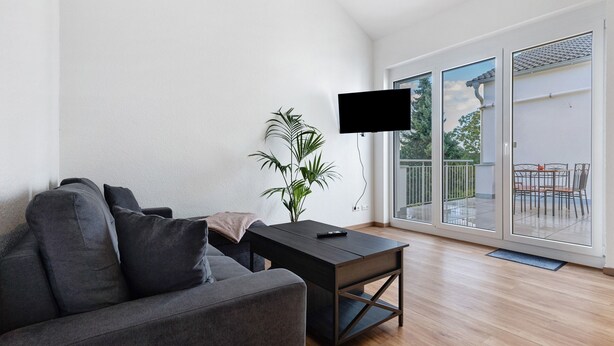 A modern living room with a sofa, a coffee table, a plant, and a TV mounted on the wall.