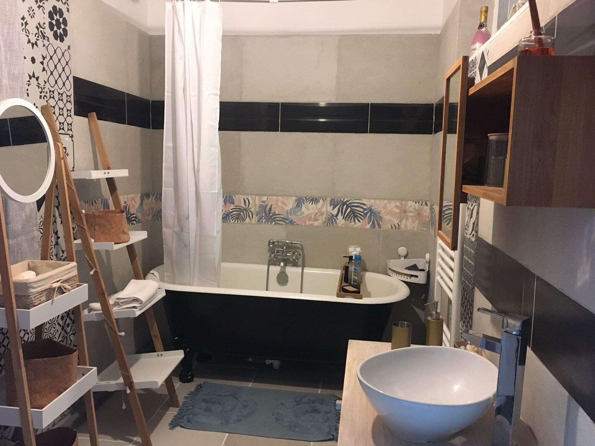 A modern bathroom with a freestanding bathtub, a large white basin, a wooden ladder shelf, and a mirror.