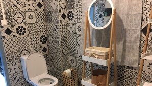 Une salle de bain avec des toilettes, des carreaux décorés, un miroir, des étagères avec des paniers et un porte-serviettes mural.
