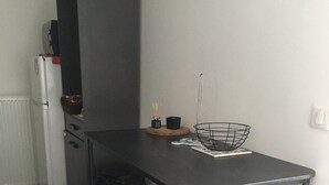 Une cuisine de taille réduite avec une table noire, deux tabourets de bar noirs, un panier en fil métallique noir et un réfrigérateur blanc.