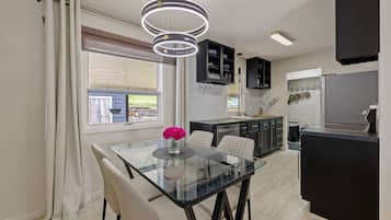 A modern kitchen with a glass dining table, black cabinets, and a hanging light fixture.