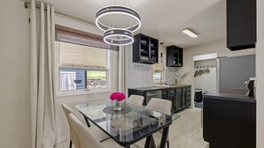 Une cuisine moderne avec une table à manger en verre, des meubles de rangement noirs et un luminaire suspendu.