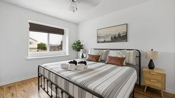 A bedroom with a bed, a nightstand, a lamp, a window, and a painting on the wall.