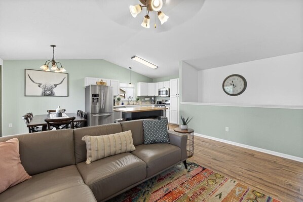 A modern living room with a sofa, a dining table, and a kitchen in the background.