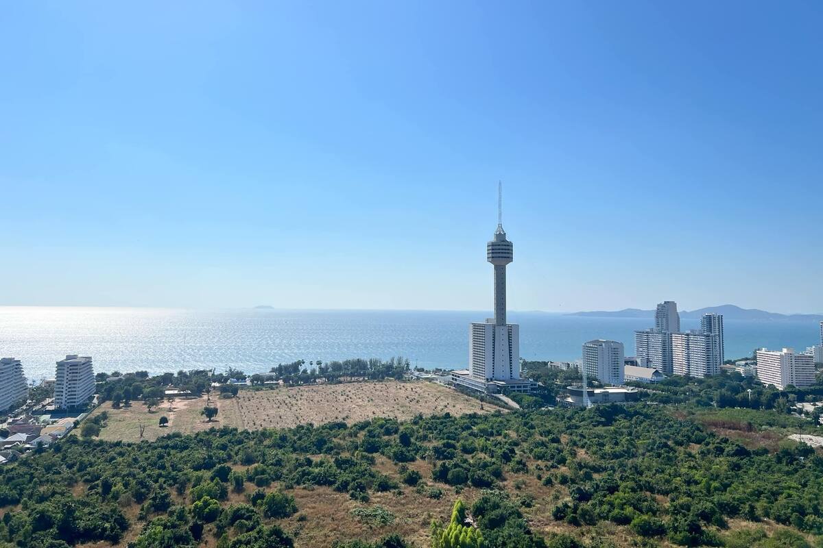 A coastal cityscape with a prominent tower, dense greenery, and high-rise buildings.