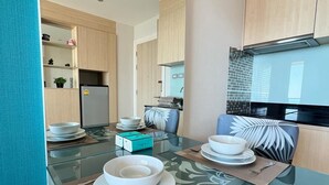 A modern kitchen with a glass dining table, wooden cabinets, and a built-in microwave. - Grande Carribean Condo By Thita (Pattaya)