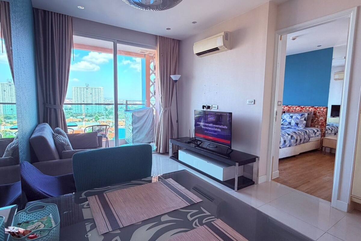 A modern living room with a sofa, a TV, and a balcony with a view of the city.