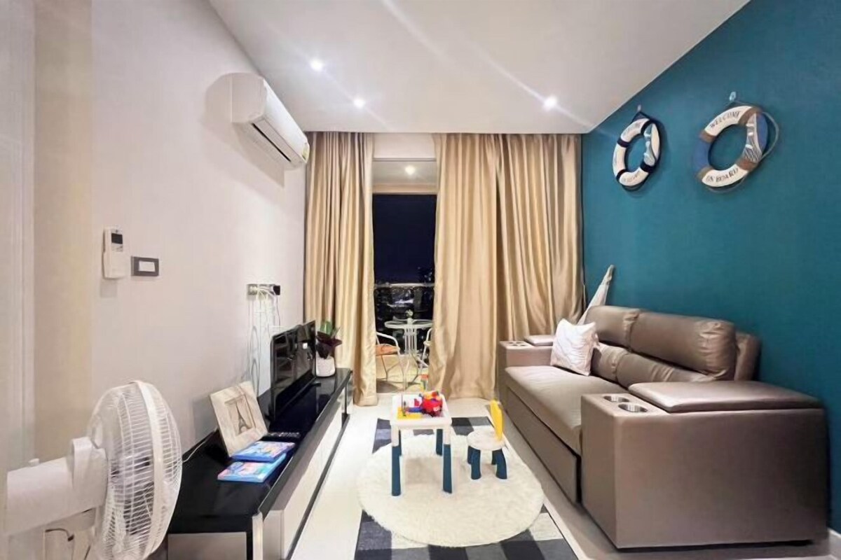 Un salon moderne avec un canapé, une petite table, un ventilateur et une vue sur l’extérieur.