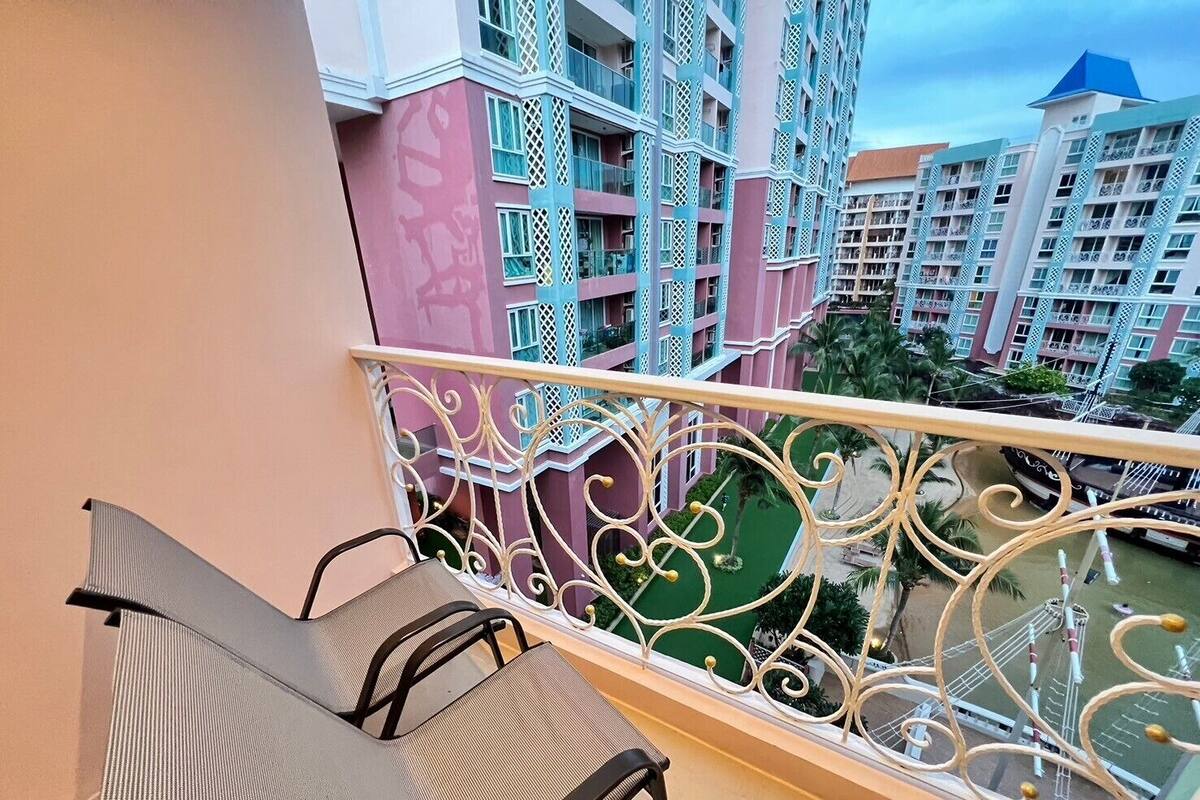 A balcony with two chairs, a decorative railing, and a view of multi-story buildings with balconies.