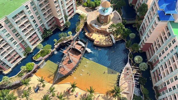 A high-rise hotel with multiple balconies, a central water feature, and a surrounding pool area. - Grande Carribean Condo By Thita (Pattaya)