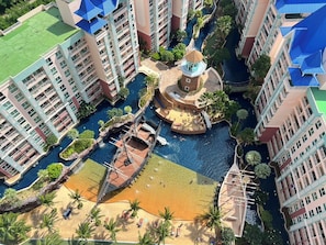 A high-rise hotel with multiple balconies, a central water feature, and a surrounding pool area. - Grande Carribean Condo By Thita (Pattaya)