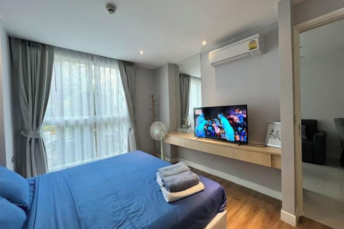 Une chambre d’hôtel avec un lit, un téléviseur posé sur un meuble, un ventilateur et une fenêtre avec des rideaux.