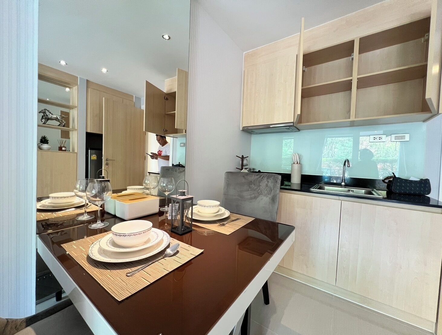 A modern kitchen with wooden cabinets, a dining table set for four with plates, glasses, and cutlery.