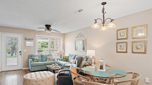 A living room with a sofa, ottoman, wicker chairs, a glass table, and a ceiling fan. - STEPS to Beach! 2B/2B, Sleeps 9! Beach, POOL, Repeat! NEW! Grill! Wagon! (Panama City Beach)
