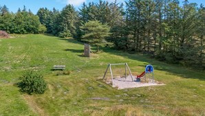 A playground with a swing set and slide, surrounded by grass and trees.