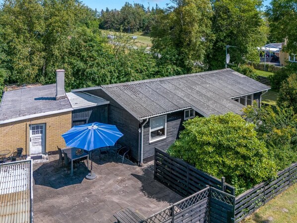 A two-story building with a sloped roof, a patio area with a blue umbrella, and a wooden fence surrounding the property.
