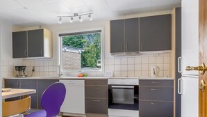 A modern kitchen with grey cabinets, a dishwasher, an oven, and a window with a view of greenery.