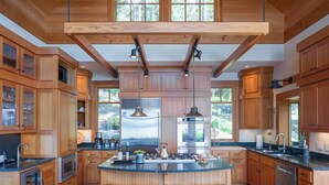 A spacious kitchen with wooden cabinetry, a central island with stools, and large windows offering views of the outdoors.