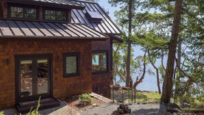 A modern house with a metal roof, large windows, and a view of a lake.