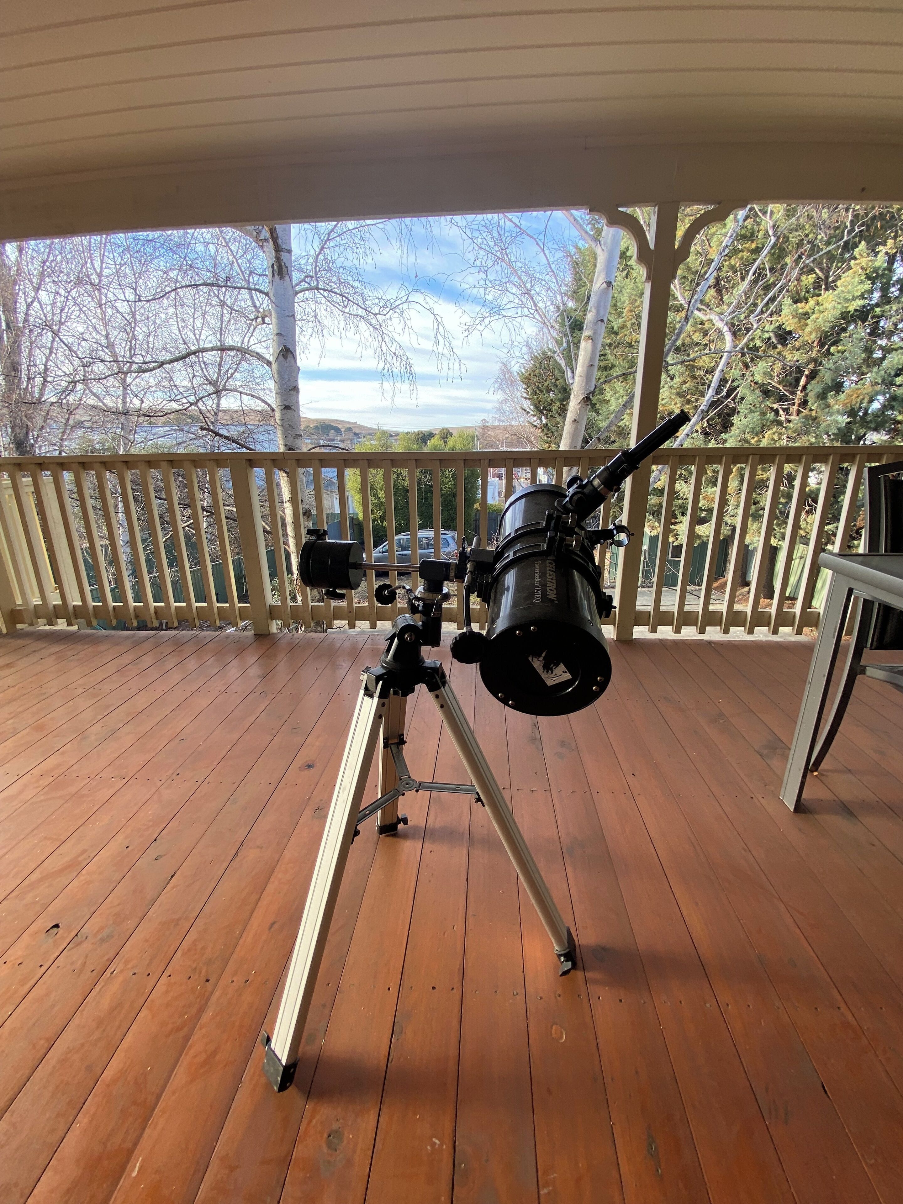 Un telescopio su un pontile di legno con ringhiera, affacciato su una zona residenziale.