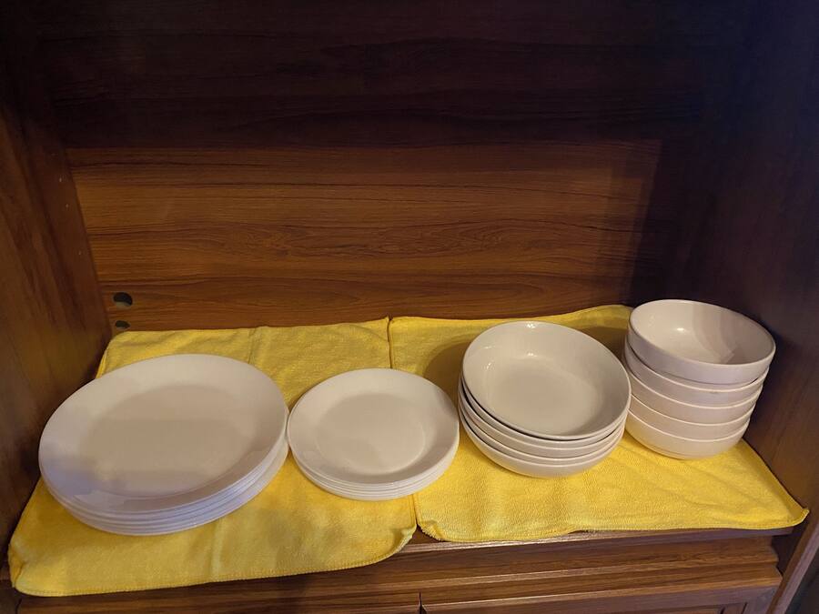 A wooden cabinet with a yellow cloth inside, containing stacks of white plates and bowls.