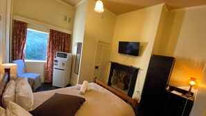 Habitación de hotel con cama, escritorio con computadora, televisor, chimenea y ventana con cortinas.