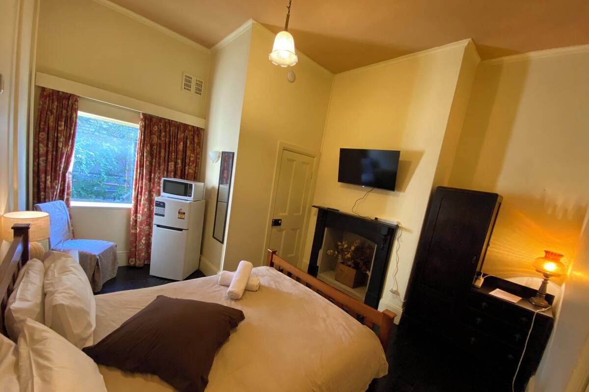Habitación de hotel con cama, escritorio con computadora, televisor, chimenea y ventana con cortinas.