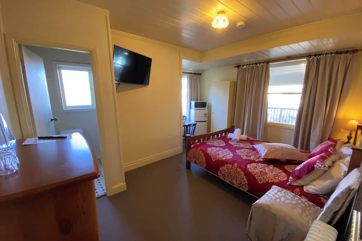 Un dormitorio con cama, mesita de noche y televisor montado en la pared.